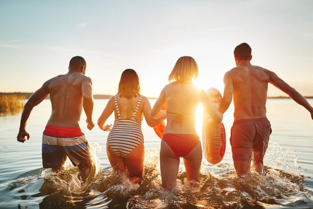 Young friends in swimsuits running into a lake at sunset